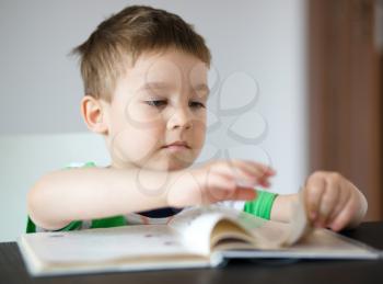 Cute little boy is reading book while sitting at table