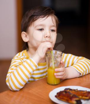 Little boy is drinking orange juice using straw