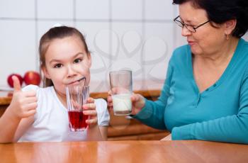 Grandmother with her grandchildren drink fruit juice, indoors