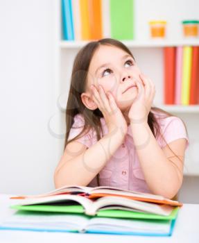 Cute little girl is reading book while sitting at table, indoor shoot