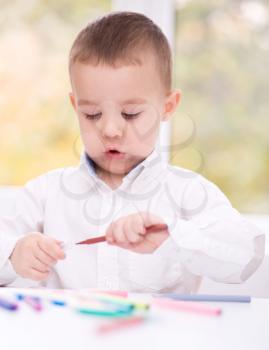 Little boy is drawing on white paper using color pencils