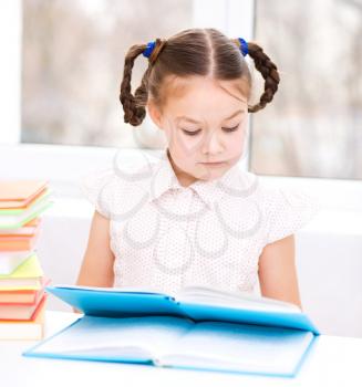 Cute little girl is reading book while sitting at table, indoor shoot