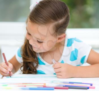 Little girl is drawing using color pencils while sitting at table