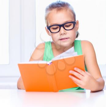 Cute little girl is reading book while sitting at table, indoor shoot