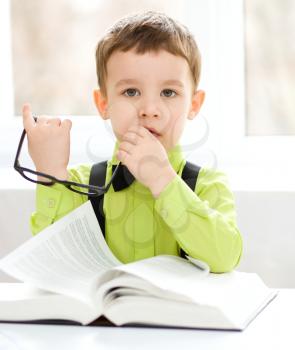 Cute little boy is reading book while sitting at table, indoor shoot