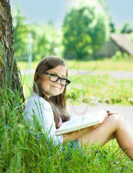 Cute little girl is reading a book outdoors