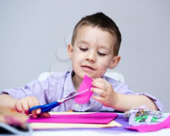 Little smiling boy is cutting paper using scissors