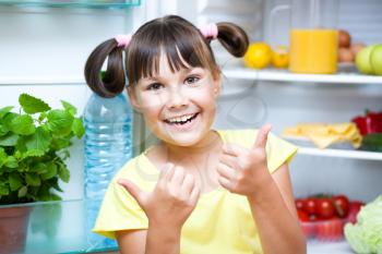 Happy girl standing near refrigerator with fruits and vegetables