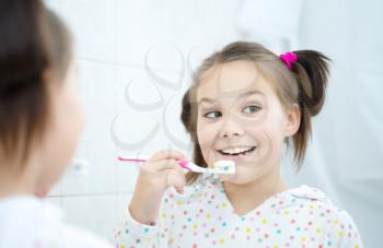 Cute happy girl brushes her teeth in the bathroom