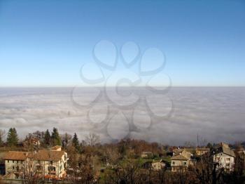 Thick fog in mountains of Italy. Mist covers valley of a small village. Mountain landscape in fog.