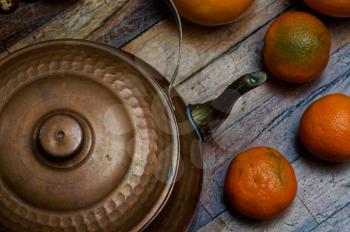 Vintage still life in dark colors. Iron kettle with orange oranges on the scratched boards.