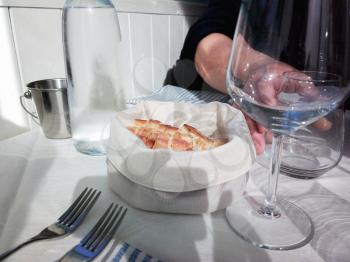 Slices of bread in a white basket and glasses of water. Freshly baked and fragrant bread on the table in the restaurant. Italy