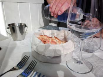Slices of bread in a white basket and glasses of water. Freshly baked and fragrant bread on the table in the restaurant. Italy