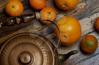Vintage still life in dark colors. Iron kettle with orange oranges on the scratched boards.