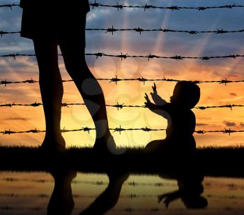 Refugee family concept. Silhouette of the child and refugee mothers legs near the fence of barbed wire