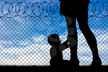 Refugee family concept. Silhouette of the child and refugee mothers legs near the fence of barbed wire