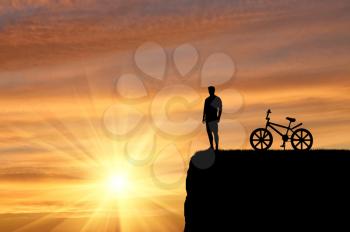 Tourism and sport concept. Silhouette of a traveler with a bicycle admiring the sunset on the top