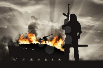 Terrorism and conflict. Armed terrorist on the background of a burning tank