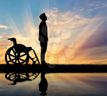 Concept of disability and disease. Silhouette of disabled person who stood out of the wheelchair at sunset and reflection in water