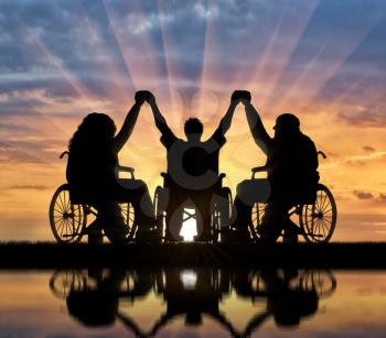 Invalids on wheelchair stand against sunset and holding hands. Concept happy disabled