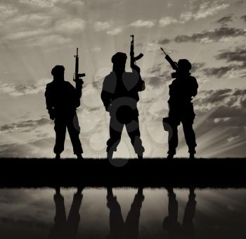 Concept of a terrorist. Silhouette of terrorists with a rifle and a reflection on the water at sunset and reflection