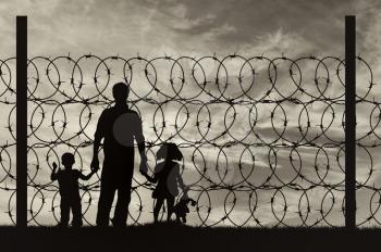 Silhouette of a family with children of refugees and fence with barbed wire on the background of the beautiful sky