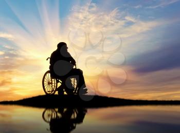 Concept of disability and old age. Silhouette of disabled person in a wheelchair at sunset and reflection in water