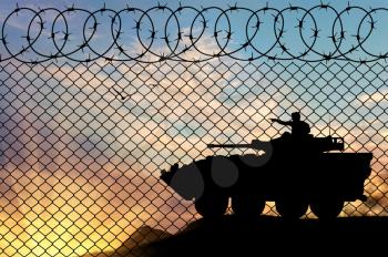 Concept of war. Silhouette Military armored personnel carrier at sunset near the fence