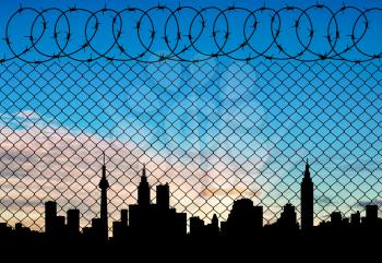 Concept of a border zone. Silhouette of the city behind a fence topped with barbed wire against a beautiful sky