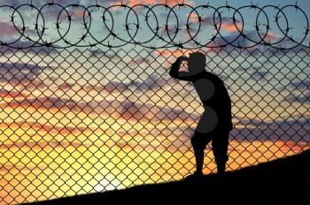 Concept of refugee. Silhouette of refugee near the border fence in the sunset