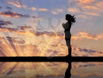 Concept of meditation and relaxation. Silhouette of a girl practicing yoga at sunset and reflection in water