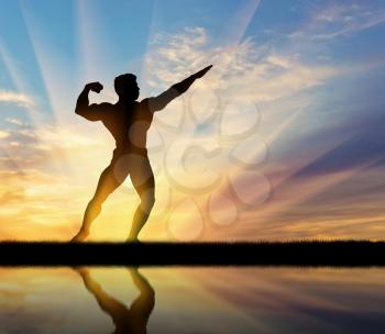 Concept of beauty and sports. Silhouette of bodybuilder posing at sunset and its reflection in water