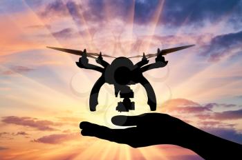 Silhouette of the landing drone on human hand on a sunset background