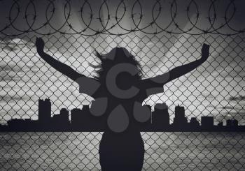 Concept of refugee. Silhouette of a woman refugee near the border on the background of the city in the distance