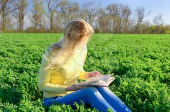 Blond woman reading a book in a green field