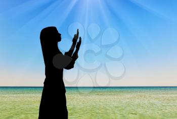 Concept of Islamic culture. Silhouette of praying woman against the sea in the rays