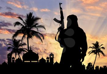 Silhouette of a terrorist with weapons near the town hall at sunset