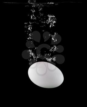 White egg falls into the water isolated on a white background