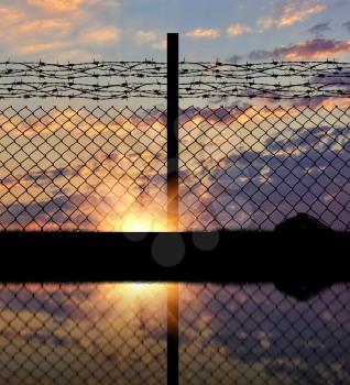 Concept of security. Silhouette of a metal fence with barbed wire on the background of sunset