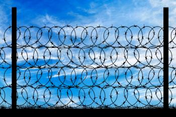Concept of security. Silhouette of a metal fence with barbed wire on the background of the beautiful sky