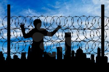 Safety concept. Silhouette of a refugee near the fence of barbed wire on the background of the city away
