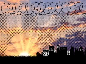 Concept of the refugees. Silhouette of a hole in the fence of barbed wire on the background of evening city
