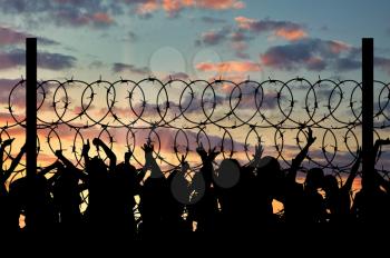 Concept of security. Silhouette of refugees climb over the barbed wire at the border