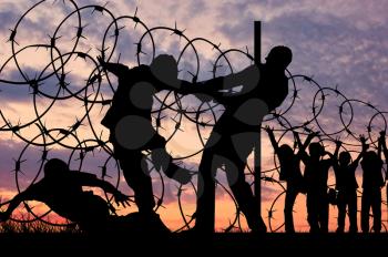  Concept of security. Silhouette of refugees climb over the barbed wire at the border