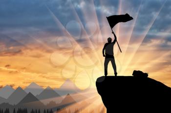 Silhouette of a climber on a mountain top with a flag in his hand. ?oncept of power and success