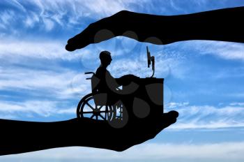 The employee is a disabled person in a wheelchair working with a computer at the table, he is in the hands of man. The concept of protection of the rights of persons with disabilities for employment