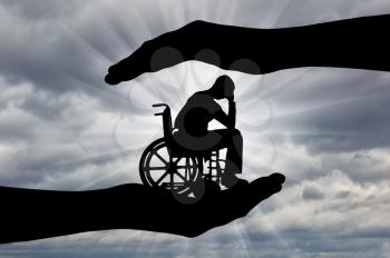 Silhouette of sad disabled man in wheelchair in hands of help. The concept of protection and assistance to people with disabilities