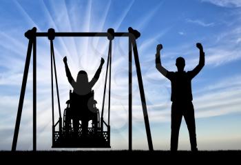 Silhouette of a happy couple, a woman wheelchair user on an adaptive swing and a healthy man nearby. Concept of the lifestyle of people with disabilities