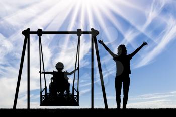 Happy child is disabled in a wheelchair on an adaptive swing for disabled children with mom. Lifestyle and support for disabled children