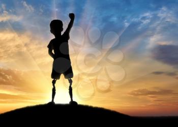 Children with disabilities concept. Happy disabled boy with a prosthetic leg standing on top of a hill at sunset